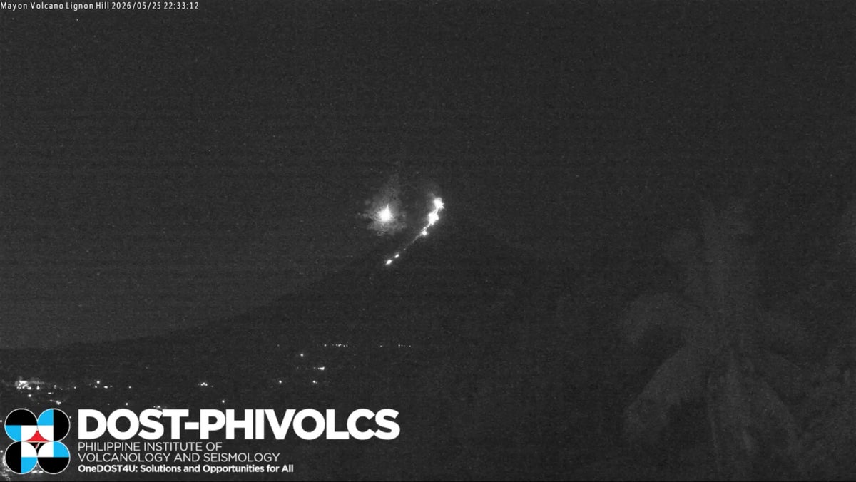 Moment meteor flies through sky beside erupting volcano