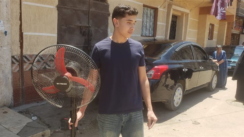 شاب يحضر مروحة لشقيقته أمام لجنة الثانوية العامة بالبحيرة لمواجهة حرارة الطقس